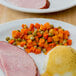 A plate of food with a fried egg and ham and a side of sweet peas and diced carrots.