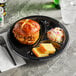 A sandwich and cornbread on a Huhtamaki Chinet black plastic 3 compartment plate.