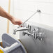 A hand using a tool to install a Chicago Faucets wall-mounted sink faucet over a grey sink.
