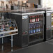 An Avantco back bar cooler on a counter filled with bottles of beer and liquor.