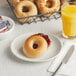 A wire basket of The Greater Knead plain bagels on a table with a plate of bagels and jam next to a glass of orange juice.