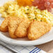 A plate of food with Lamb Weston triangle hash brown patties, chicken nuggets, and fruit on a table.