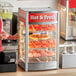 A woman standing in front of a ServIt countertop hot food display with pizza on the shelves.