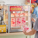A person using a ServIt countertop popcorn display case to get popcorn from a box.