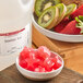 A bowl of strawberries and a kiwi next to a bottle of strawberry kiwi flavored liquid.