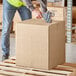 A person using tape to seal a Lavex kraft shipping box.