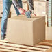 A person holding a Lavex Kraft corrugated shipping box.