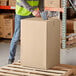 A man wearing a safety vest moving a Lavex Kraft shipping box.