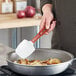 A hand using a red Vollrath SoftSpoon to cook onions in a pan.