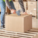 A person using a box cutter to cut a Lavex Kraft shipping box.