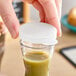 A hand holding a white plastic lid on a plastic beverage decanter filled with a green liquid.