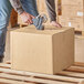 A person using a box cutter to cut a Lavex cardboard shipping box.