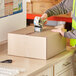 A person using a tape gun to seal a Lavex shipping box.