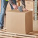 A man in a yellow vest packing a Lavex cardboard shipping box.