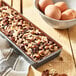 A de Buyer rectangular stainless steel tart mold with a non-stick sheet on a counter next to a bowl of eggs.