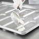 A person pouring white liquid into a Chicago Metallic rounded end hoagie bun pan.
