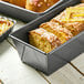 A de Buyer non-stick iron loaf pan with a loaf of bread inside on a table.