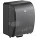 A black Tork mechanical paper towel dispenser with a clear glass door.