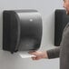 A man using a black Tork mechanical paper towel dispenser.