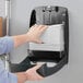 A hand putting Tork Universal white multi-fold paper towels in a wall mounted dispenser.