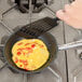 A hand using a spatula to cook an omelette in a Vollrath Optio stainless steel non-stick fry pan.