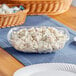 A clear PET plastic square bowl filled with potato salad on a table.