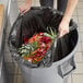 A woman putting a Lavex trash bag full of food into a trash can.