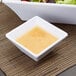 A white square GET Melamine bowl with salad next to a bowl of dressing.