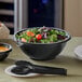 A black Visions catering bowl filled with salad and a spoon.