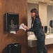 A black Tork Peakserve Mini Continuous Paper Towel Dispenser mounted on a restroom wall.