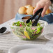 A hand using tongs to serve salad from a Visions plastic bowl.