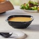 A Visions black plastic square bowl filled with soup on a table.