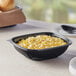 A Visions black PET plastic bowl filled with macaroni and cheese on a table with a spoon.