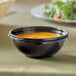 A Visions black plastic bowl of soup on a table.