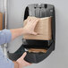 A hand putting Tork multi-fold paper towels in a wall-mounted dispenser.