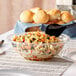 A Visions clear plastic round catering bowl filled with pasta, black beans, and tomatoes, with a spoon in it.