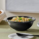 A Visions black plastic bowl filled with food on a table.