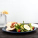 A Carlisle Dallas Ware cafe blue melamine plate with a sandwich and salad on it on a table.