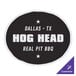 A black and white rectangular sticker with white text that reads "Dallas Texas" and "Hog Head Real Pit Bull" on a table in a butcher shop.