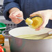 A person pouring yellow powder from a container into a bowl of food.