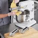 A chef using an Avantco pasta roller and cutter attachment kit on a silver and black Avantco mixer.