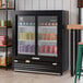 A black refrigerated sliding glass door merchandiser with LED lighting, stocked with assorted canned beverages.