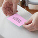 A person's hands using a Lavex purple thermal label on a pink piece of paper.