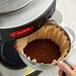 A person pouring Crown Beverages Emperor's Finest coffee into a coffee maker.