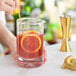 A person using a Barfly stirring glass to mix a drink with a straw and a slice of orange.