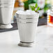 A Barfly stainless steel mint julep cup on a marble surface filled with ice and mint leaves.