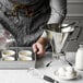 A person using a de Buyer stainless steel piston funnel to pour yellow liquid into small cups.