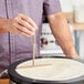 A person using a de Buyer beechwood crepe batter spreader to make a crepe in a pan.