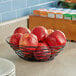 A Tablecraft black wire basket filled with red apples on a counter.