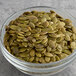 A glass bowl of Bob's Red Mill Raw Organic Pumpkin Seeds on a table.